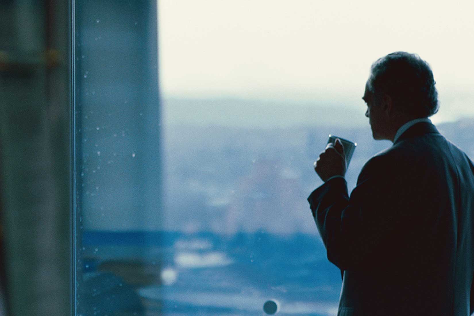Man in suit looking out window drinking coffee