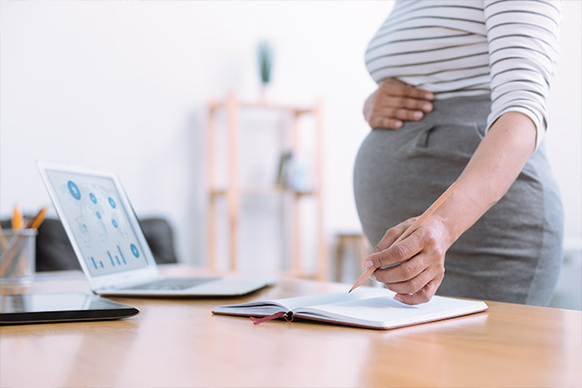Pregnant female employee holding belly reviewing FMLA leave management documents